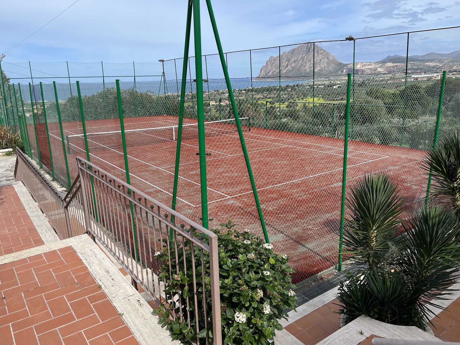 Red clay tennis court with Monte Cofano beyond the fence